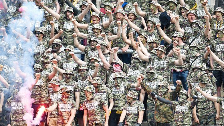 Dresdener Fans in Tarnkleidung stehen während des Spiels auf der Tribüne. Fanproteste werden immer radikaler. Foto: Uwe Anspach/dp