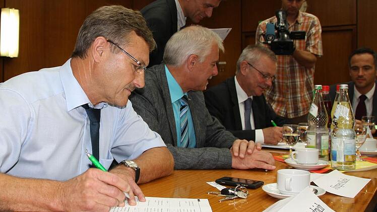 Während der Oberthulbaer Bürgermeister Gotthard Schlereth (hinten) die englische Version des Erweiterungsvertrages einfach unterzeichnete, fügte sein Zeitlofser Amtskollege Wilhelm Friedrich (vorne) seiner Unterschrift eine Einschränkung seines Gemeinderates an. In der Mitte Jürgen Karle, Wartmannsroth.