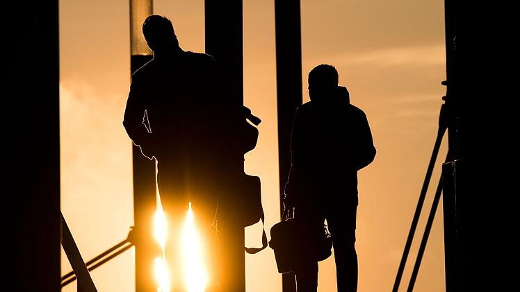 Zwei M&auml;nner gehen mit Aktentasche bei Sonnenaufgang &uuml;ber Br&uuml;cke