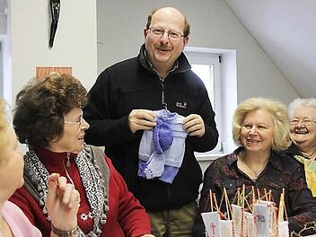 Pfarrer Christian Müssig bewundert die wollenen Kinderkleidchen, welche die fleißigen Frauen hergestellt haben. Der 1976 begründete Bastelkreis hat im Laufe der Jahre über 100.000 Euro aus dem Verkauf der Sachen für gute Zwecke gespendet. Foto: Gerd Schaar