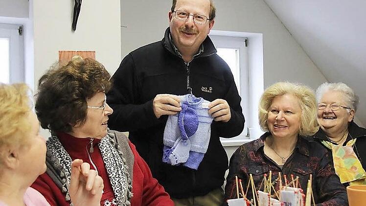 Pfarrer Christian Müssig bewundert die wollenen Kinderkleidchen, welche die fleißigen Frauen hergestellt haben. Der 1976 begründete Bastelkreis hat im Laufe der Jahre über 100.000 Euro aus dem Verkauf der Sachen für gute Zwecke gespendet. Foto: Gerd Schaar