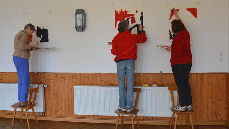 Die Kreuzwegstationen, die Ursula Hoos, Sabine Halbritter und Helma Schug an die Wand pinseln stammen, von einem amerikanischen Künstler. Wie der gesamte Raum sind sie in den Farben rot, schwarz und weiß gehalten. Foto: Berthold