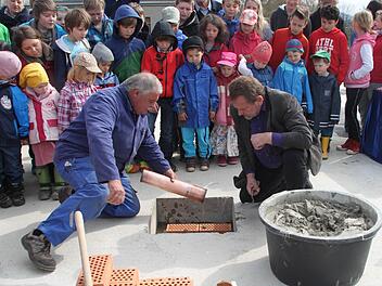 Ein Kupferrohr mit Geld, Zeichnungen und einer Seite der Bayerischen Rundschau wurde bei der Grundsteinlegung mit in die Bodenplatte eingemauert. Gespannt verfolgen die Kinder die Arbeit von Josef Witzgall von der Firma Mattis (links) und Joachim Gutschmidt vom Vorstand der Waldorfschule. Foto: Jürgen Gärtner.