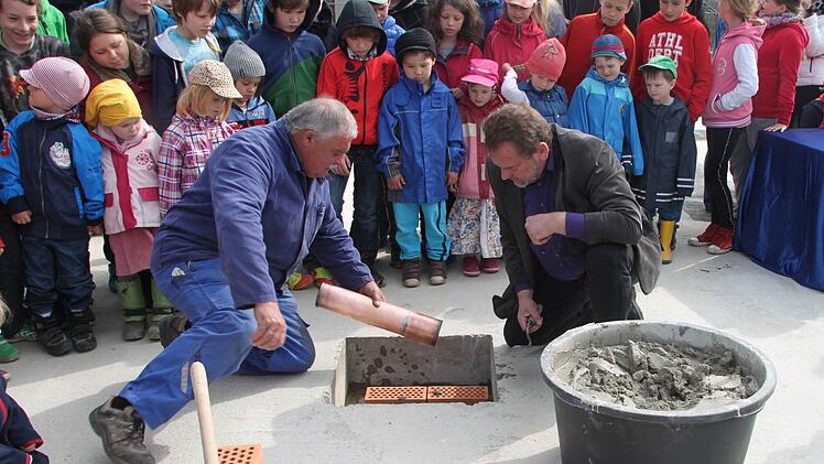 Ein Kupferrohr mit Geld, Zeichnungen und einer Seite der Bayerischen Rundschau wurde bei der Grundsteinlegung mit in die Bodenplatte eingemauert. Gespannt verfolgen die Kinder die Arbeit von Josef Witzgall von der Firma Mattis (links) und Joachim Gutschmidt vom Vorstand der Waldorfschule. Foto: Jürgen Gärtner.