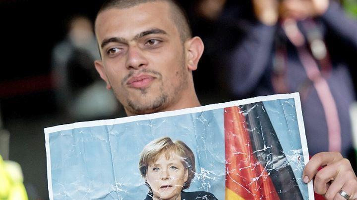 Ein Flüchtling, der kurz zuvor mit einem Zug angekommen ist, hält am 5. September 2015 auf dem Hauptbahnhof in München ein Foto von Angela Merkel in den Händen. Foto: Sven Hoppe, dpa