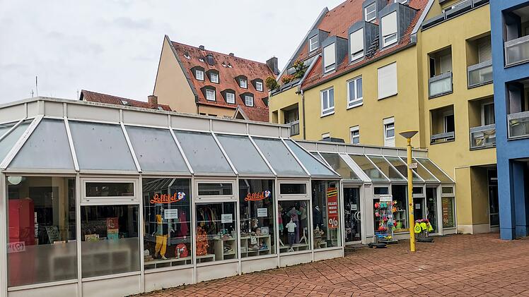 Ein Laden in Bamberger Innenstadt schlie&szlig;t nach 14 Jahren. Schaufenster zeigt Kindermode und Rabatt-Schilder. Geb&auml;ude mit gelben und blauen Fassaden, gepflasterter Platz davor.