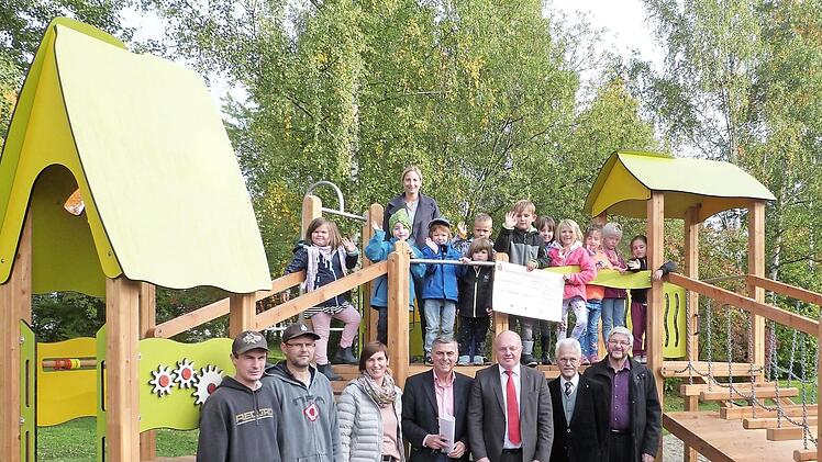 Die Kids mit Kita-Leiterin Sylvia Düreth stehen auf dem neuen Spielgerät, die Offiziellen davor. Im Bild (von links) die Bauhofmitarbeiter Sebastian Hahn und Sven Schmidt, Sandra Schmidt von der Verwaltung, Bürgermeister Siegfried Decker, Bernd Sesselmann und Gunter Heckel vom Lions-Club sowie Pfarrer Stefan Schleicher. Foto: Werner Reißaus