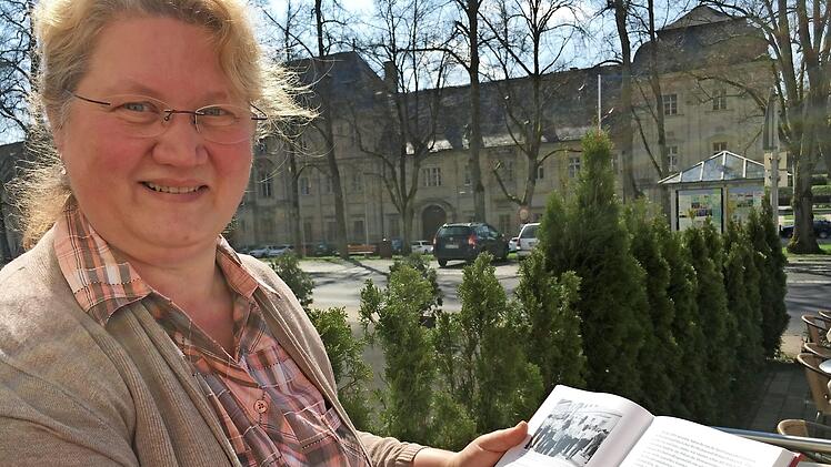 Ebrachs Gemeindearchivarin Barbara G&uuml;lta bl&auml;ttert in einem Ebrach-Buch, im Hintergrund das Gef&auml;ngnis. Foto: Anette Schreiber