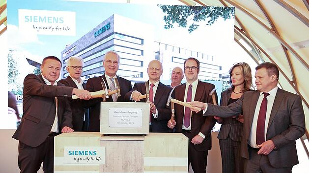 Siemens-Betriebsratsvorsitzender Erlangen-S&uuml;d, Manfred B&auml;reis, Architekt J&uuml;rgen Engel, Staatsminister Joachim Herrmann, Siemens-Vorstand Ralf Thomas, General&uuml;bernehmer Kurt Zech, Oberb&uuml;rgermeister Florian Janik, Betriebsratsvorsitzende Erlangen-Mitte, Saskia Krausser, und Zsolt Sluitner, CEO Siemens Real Estate (v. l.), best&uuml;cken die Zeitkapsel f&uuml;r den Grundstein. Foto: Siemens