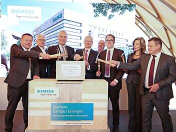 Siemens-Betriebsratsvorsitzender Erlangen-Süd, Manfred Bäreis, Architekt Jürgen Engel, Staatsminister Joachim Herrmann, Siemens-Vorstand Ralf Thomas, Generalübernehmer Kurt Zech, Oberbürgermeister Florian Janik, Betriebsratsvorsitzende Erlangen-Mitte, Saskia Krausser, und Zsolt Sluitner, CEO Siemens Real Estate (v. l.), bestücken die Zeitkapsel für den Grundstein. Foto: Siemens