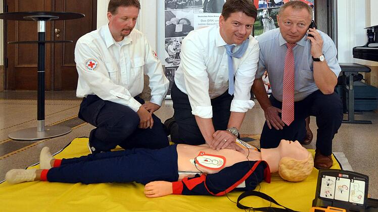 Unter fachkundiger Leitung "reanimiert" hier MdL Sandro Kirchner eine Übungspuppe. Auf unserem Foto (von links): Rotkreuz-Ausbilder Thomas Menz, MdL Sandro Kirchner und Landrat Thomas Bold, der direkt von der Rettungsleitstelle per Handy die richtigen Reanimationshinweise bekommt und an weitere Helfer weitergibt. Foto: Peter Rauch