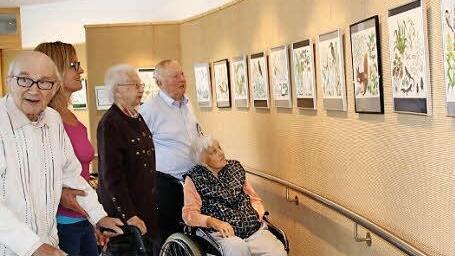 Besucher und Heimbewohner betrachten die farbigen Kalenderblätter aus den 1950er Jahren, die derzeit in der Kleinen Galerie des Seniorenzentrums ausgestellt sind. Foto: Heike Beudert