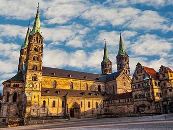 Der Bamberger Dom im Sonnenschein mit seinen markanten T&uuml;rmen vor einem teilweise bew&ouml;lkten Himmel. Historische Architektur im Vordergrund.