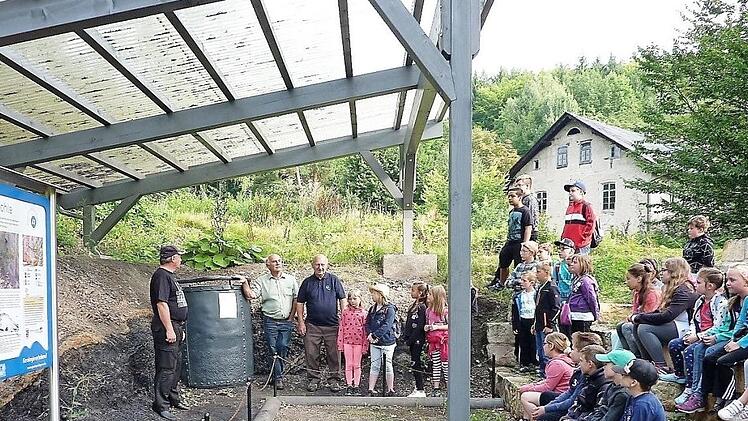 Buben und Mädchen blicken in die Vergangenheit der Bergleute: Unser Bild zeigt das überdachte Stockheimer Geotop mit dem zehn Zentner schweren Teufkübel, im Hintergrund die bergmännische Rentei von 1870 sowie (v. l.) Detlef Heublein, Gerwin Eidloth und Willi Müller.  Foto: Gerd Fleischmann