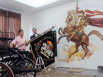 Unter den Hufen von Florians Pferd ist die brennende Pfarrkirche im Entstehen. Zweiter Kommandant Robert Bank (rechts) und Bürgermeister Carsten Joneitis halten die Jubiläumsfahne, die Vorlage für  das Kunstwerk ist.  Foto: Anette Schreiber