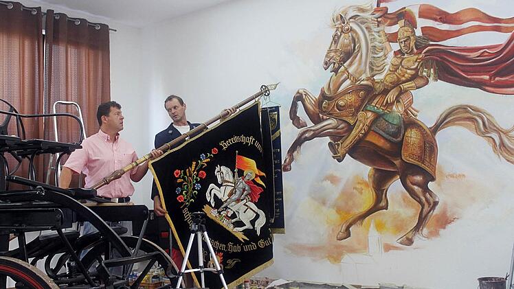 Unter den Hufen von Florians Pferd ist die brennende Pfarrkirche im Entstehen. Zweiter Kommandant Robert Bank (rechts) und Bürgermeister Carsten Joneitis halten die Jubiläumsfahne, die Vorlage für  das Kunstwerk ist.  Foto: Anette Schreiber