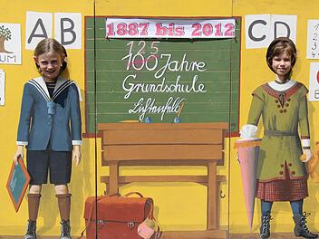Beim Schulfest steckten zwei Mädchen ihre Köpfe durch eine Wand, auf der eine historische Schulumgebung dargestellt ist. Damit machte die Schule auf ihr Jubiläum aufmerksam. Foto:  p