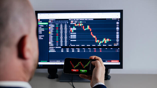 ETF B&ouml;rse Aktien Kurse Business man using a mobile device to trade stocks or currency on a financial market.  Nahaufnahme der Hand eines H&auml;ndlers, der ein Smartphone in der Hand h&auml;lt und eine Trading-App mit B&ouml;rsencharts zur Finanzanalyse und zur &Uuml;berwachung von Anlagedaten nutzt.
