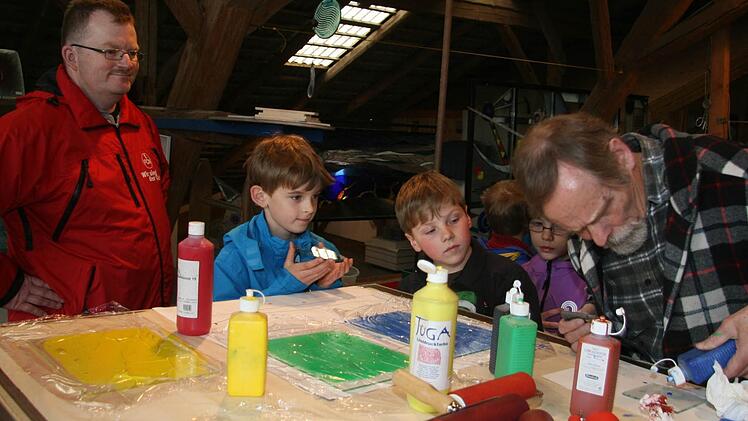 Frank Preußners (links) und die Jungschar-Kinder aus Rugendorf lassen sich von Glaskünstler Wilfried Radtke (rechts) erklären, wie Glasdruck funktioniert. Radtke bestreicht gravierte Glasplatten mit Farbe. Foto: Sonja Adam