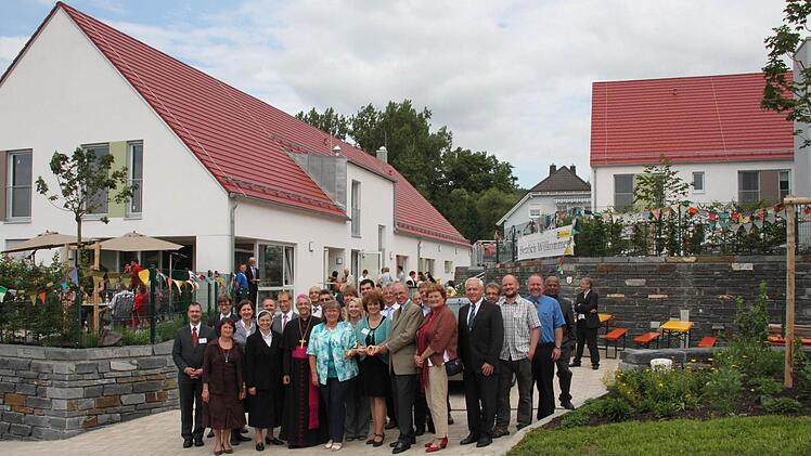 Architekt Friedrich C. Haindl (vorne, Dritter von rechts) überreicht der Leiterin von Regens Wagner, Sabine Schubert (links daneben), und ihrer Vorgängerin Maria Bauer (vorne, Fünfte von rechts), die die Idee zu der Einrichtung hatte, symbolisch einen Schlüssel. Auch Erzbischof Ludwig Schick (vorne, sechster von rechts) freut sich.