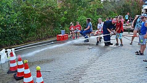 Beim Zielspritzen mit der Kübelspritze zeigten Mitglieder der Jugendfeuerwehr den Kindern, wie sie das Gerät halten müssen, damit die Tennisbälle von den Hütchen gespritzt werden.