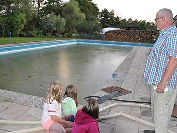 Olaf Betz, Vorsitzender des Schwimmbadvereins Kraisdorf, schaut nachdenklich auf das Schwimmerbecken, das zwar mit Wasser gefüllt, aber nicht "badesauber" ist; denn das Freibad in Kraisdorf bleibt heuer geschlossen. Auch die drei Mädchen im Vordergrund vermissen es, im Wasser zu toben. Simon Albrecht