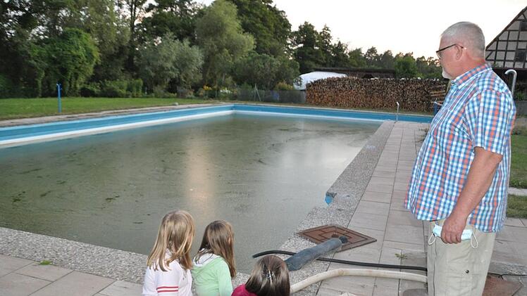 Olaf Betz, Vorsitzender des Schwimmbadvereins Kraisdorf, schaut nachdenklich auf das Schwimmerbecken, das zwar mit Wasser gefüllt, aber nicht "badesauber" ist; denn das Freibad in Kraisdorf bleibt heuer geschlossen. Auch die drei Mädchen im Vordergrund vermissen es, im Wasser zu toben. Simon Albrecht
