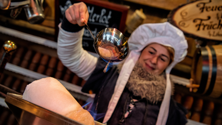 Eine Frau steht vor einer Feuerzangenbowle am Historischen Weihnachtsmarkt.