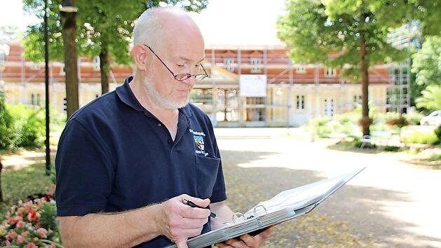 Christian Neugebauer betrachtet seine Sammlung alter Postkarten, die zeigen, wie sich die Brunnenlage im Inneren des Brunnenbaus (im Hintergrund) &uuml;ber die Jahre ver&auml;ndert hat. Foto: Charlotte Wittnebel-Schmitz