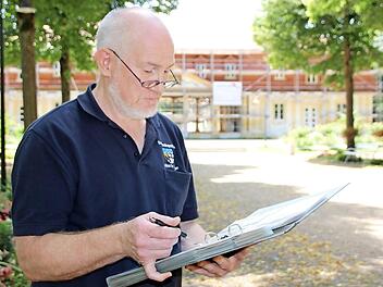 Christian Neugebauer betrachtet seine Sammlung alter Postkarten, die zeigen, wie sich die Brunnenlage im Inneren des Brunnenbaus (im Hintergrund) über die Jahre verändert hat. Foto: Charlotte Wittnebel-Schmitz