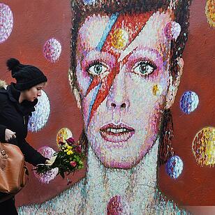 A women lays flowers at a mural of British singer David Bowie in Brixton, birth place of the late David Bowie in London, Britain, 11 January 2016. Well-wishers have flocked to the Bowie mural to pay their respects following the announcement of his death.  Foto: EPA/ANDY RAIN