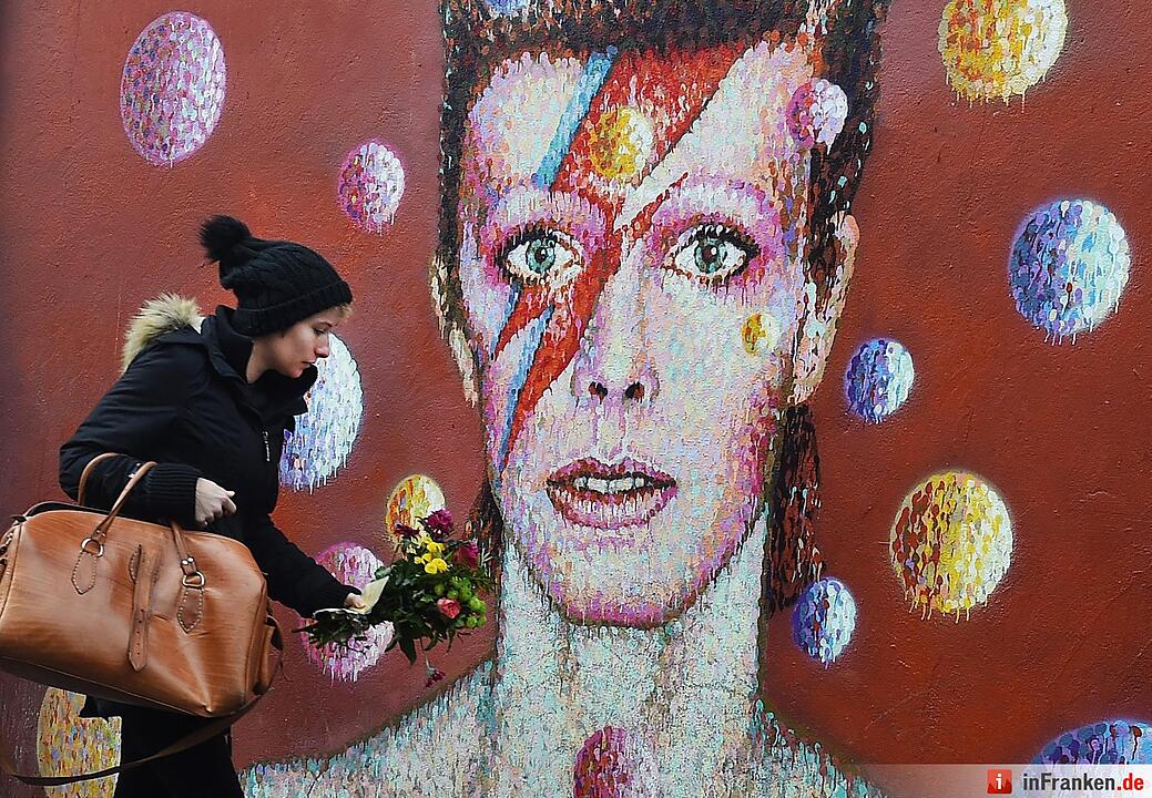 A women lays flowers at a mural of British singer David Bowie in Brixton, birth place of the late David Bowie in London, Britain, 11 January 2016. Well-wishers have flocked to the Bowie mural to pay their respects following the announcement of his death.  Foto: EPA/ANDY RAIN
