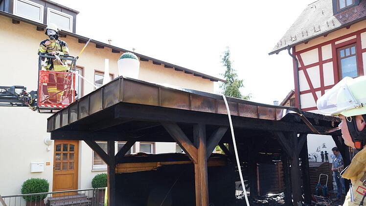 Ein Feuerwehr sucht das Dach des Carports nach Glutnestern ab.