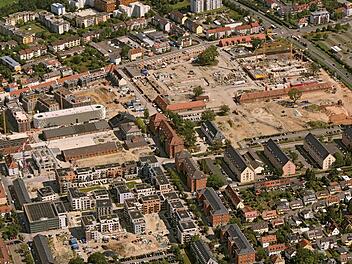 Luftaufnahme eines Stadtteils mit mehreren Baustellen, Wohngebäuden und Infrastruktur. Kräne und Bauarbeiten sind sichtbar. Veranstaltung am Lagarde-Campus in Bamberg naht.