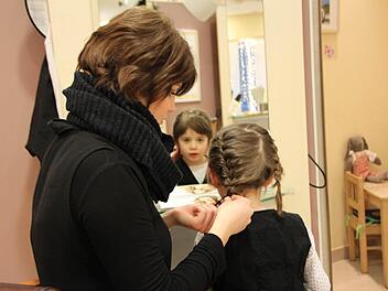 Frisiert werden wie die Großen: Die vierjährige Cara Sophia Kehm darf ausnahmsweise auf Muttis Arbeit in Bad Brückenau vorbeischauen. Viktoria Liebhardt, Auszubildende im dritten Lehrjahr, flicht ihr die Haare. Foto: Ulrike Müller