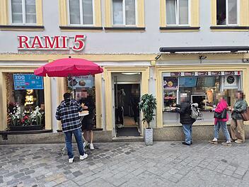 Vor einem Restaurant in Bamberg warten Menschen in einer Schlange. Ein roter Schirm steht da. Ein Schild bewirbt Gratis-Falafel in Kooperation mit Wolt.