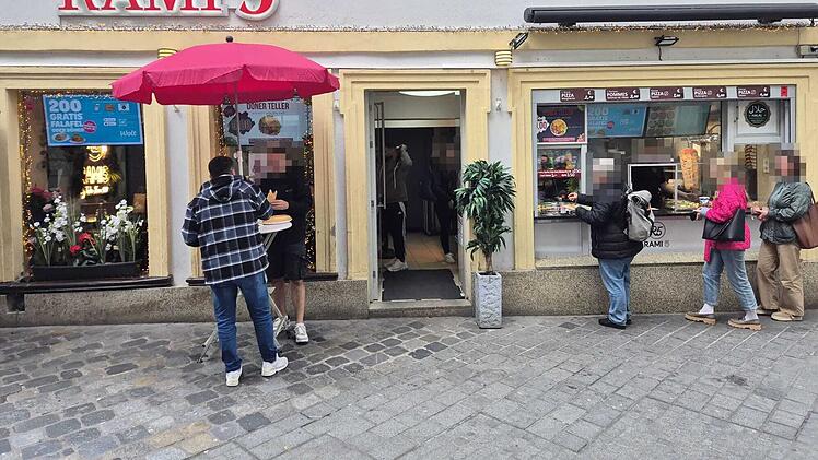 Vor einem Restaurant in Bamberg warten Menschen in einer Schlange. Ein roter Schirm steht da. Ein Schild bewirbt Gratis-Falafel in Kooperation mit Wolt.
