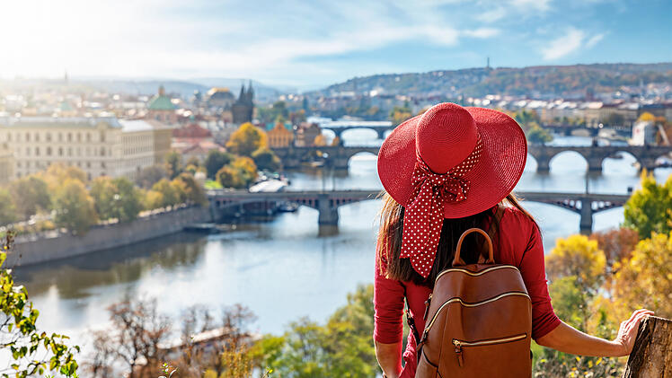 Touristin mit Hut genie&szlig;t die Aussicht auf die Karlsbr&uuml;cke und die Altstadt von Prag, Tschechiche Republik, an einem sonnigen Herbsttag