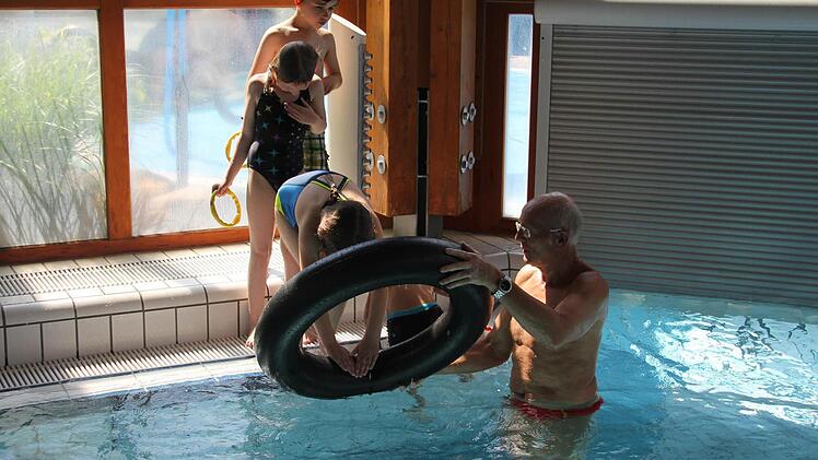Richard Bär übt mit Schülern im Crana Mare das Springen durch einen Reifen und das Aufsammeln von Ringen vom Boden des Beckens. Damit führt er sie spielerisch auf die Übungen der DLRG hin. Foto: Friedwald Schedel