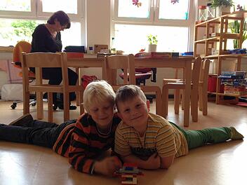 Robin (links) und Ciaron haben Freizeit und spielen mit Lego-Bausteinen auf dem Fußboden. Sie werden von Silke Helget beaufsichtigt. Foto: Alexandra Wirth
