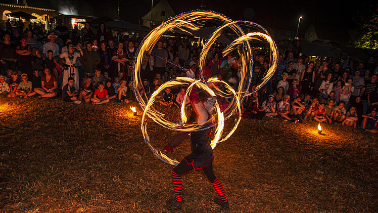 Ein Feuerspucker führt vor einem großen, gespannten Publikum eine atemberaubende Show im Dunkeln auf. Die lodernden Flammen zeichnen leuchtende Muster in die Luft.