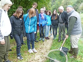Karl-Peter Schwegel (rechts) zeigt den Besuchern Regenbogenforellen. Beh&ouml;rdenleiter Schmittn&auml;gel, Landrat Dr. Ulm und Sch&uuml;lerinnen sehen interessiert zu.