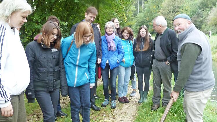 Karl-Peter Schwegel (rechts) zeigt den Besuchern Regenbogenforellen. Beh&ouml;rdenleiter Schmittn&auml;gel, Landrat Dr. Ulm und Sch&uuml;lerinnen sehen interessiert zu.