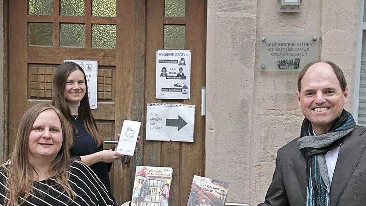 Michael Hofmann überreicht die beiden Bücher an Büchereileiterin Beate Knörlein und Sandra Adelhardt (hinten) von der Gemeindebücherei St. Bartholomäus in Kirchehrenbach.
