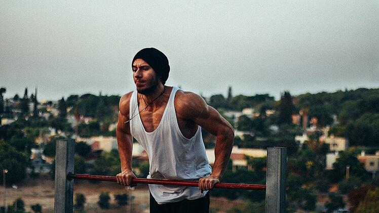Ein Sportler beim Street workout. Gleichzeitige Eiweißreiche Ernährung kann zusammen mit ausreichend Sport das gewünschte Ergebnis begünstigen.