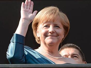 Grüße ans applaudierende Volk: Bundeskanzlerin Angela Merkel, im Hintergrund ihr Mann Joachim Sauer. Foto: Timm Schamberger/dapd