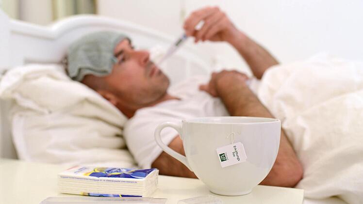 Ein kranker Mann liegt a im Bett und misst Fieber. Durch die jährliche Grippewelle haben Ärzte und Krankenhäuser in Bayern im Moment viel zu tun. Foto: Andreas Gebert/dpa