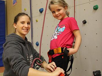 FSJ-lerin Nicole Weipert (links) legt Lenia (5) den Klettergurt an und sichert sie an der Wand ab. Foto: Benedikt Borst