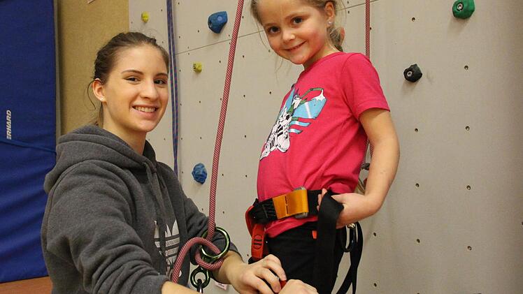 FSJ-lerin Nicole Weipert (links) legt Lenia (5) den Klettergurt an und sichert sie an der Wand ab. Foto: Benedikt Borst