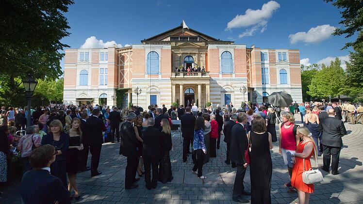 Besucher warten am 25.07.2014 bei der Eröffnung der Bayreuther Festspiele auf dem Grünen Hügel in Bayreuth bei einer unplanmäßigen Unterbrechung wegen eines technischen Defekts vor dem Festspielhaus. Die Richard-Wagner-Festspiele sind eines der wichtigsten kulturellen und gesellschaftlichen Ereignisse Deutschlands. Foto: Tobias Hase/dpa